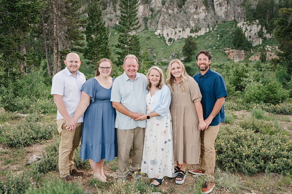 Group portrait against scenic mountain backdrop with evergreen trees and rocky cliffs.