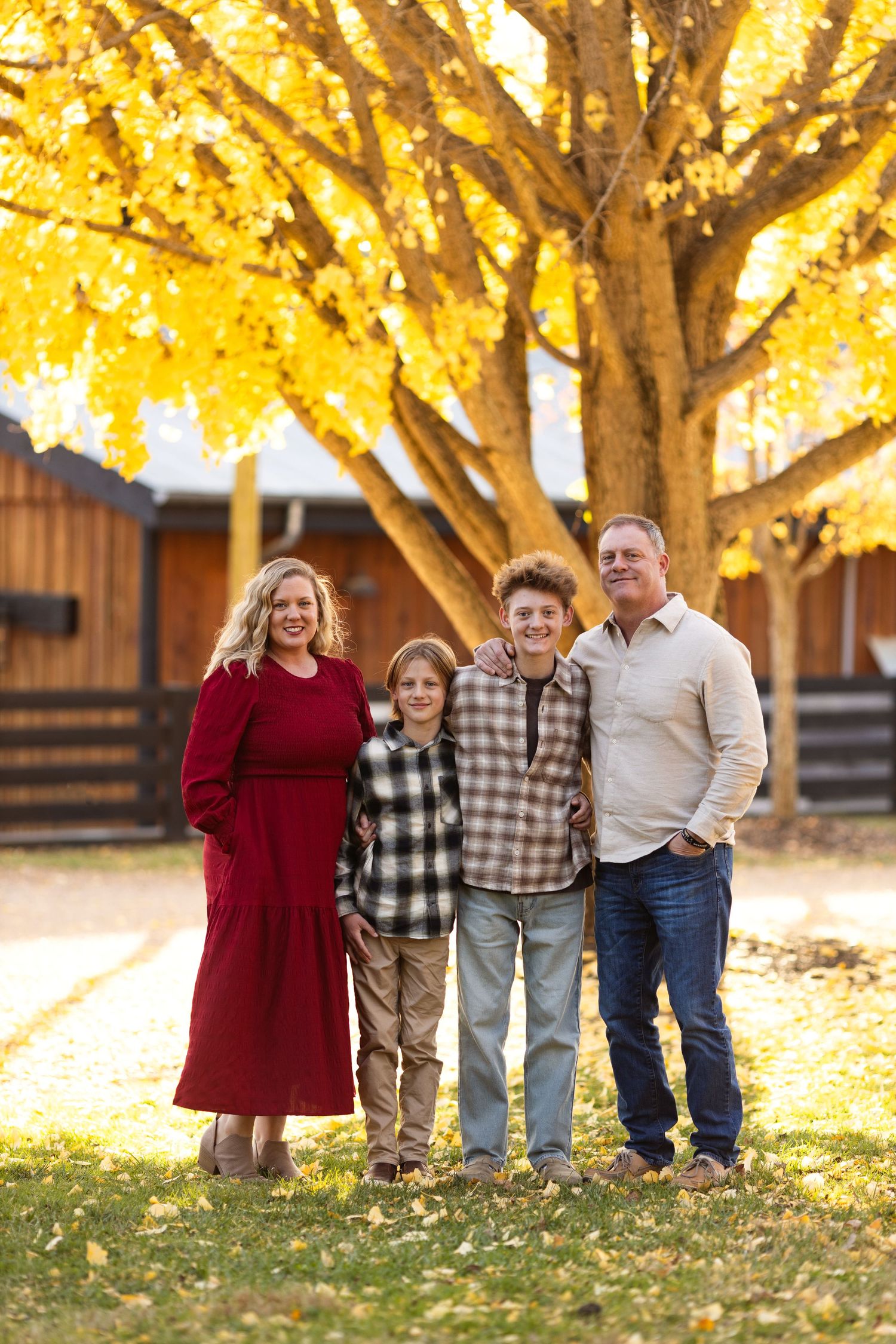 A group stands together under a golden autumn tree with fallen yellow leaves in front of a rustic wooden building.