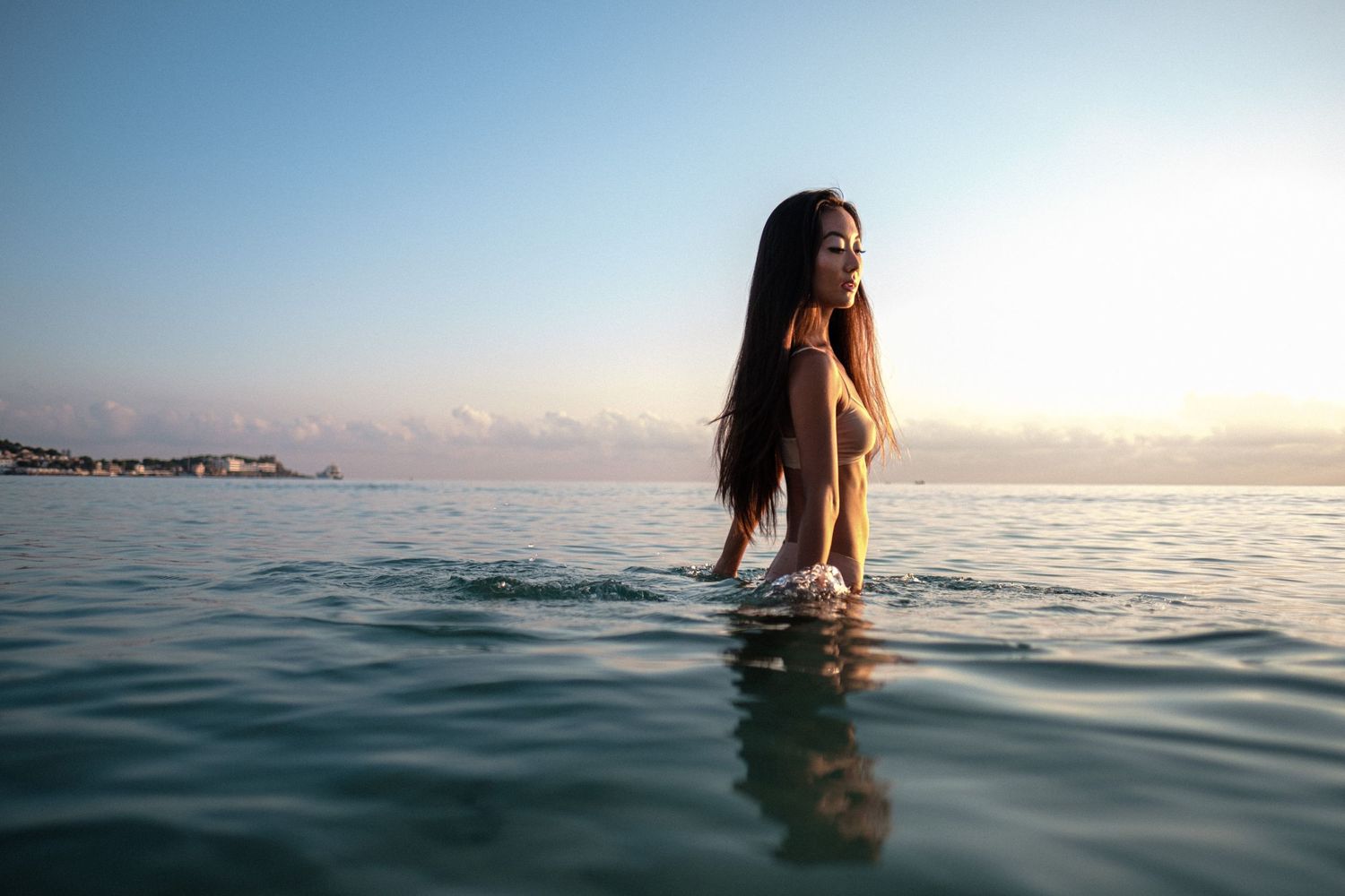 Silhouettes of people wading in calm ocean water during sunset.