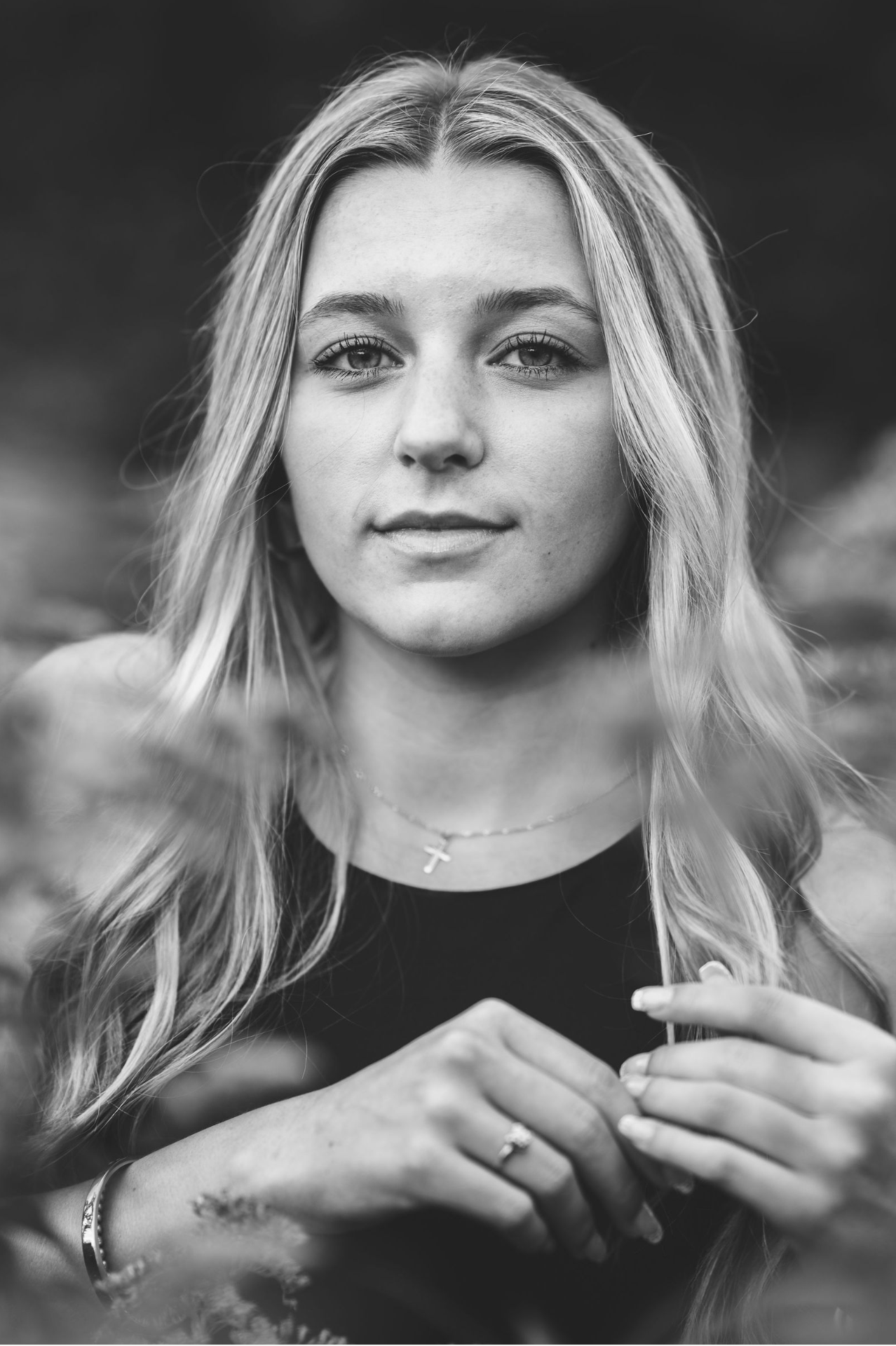 Black and white close-up portrait of young blonde woman with cross necklace and bracelet outdoors.