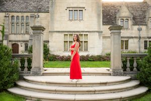 A figure in a flowing red dress poses elegantly on curved stone steps of a grand historic building.