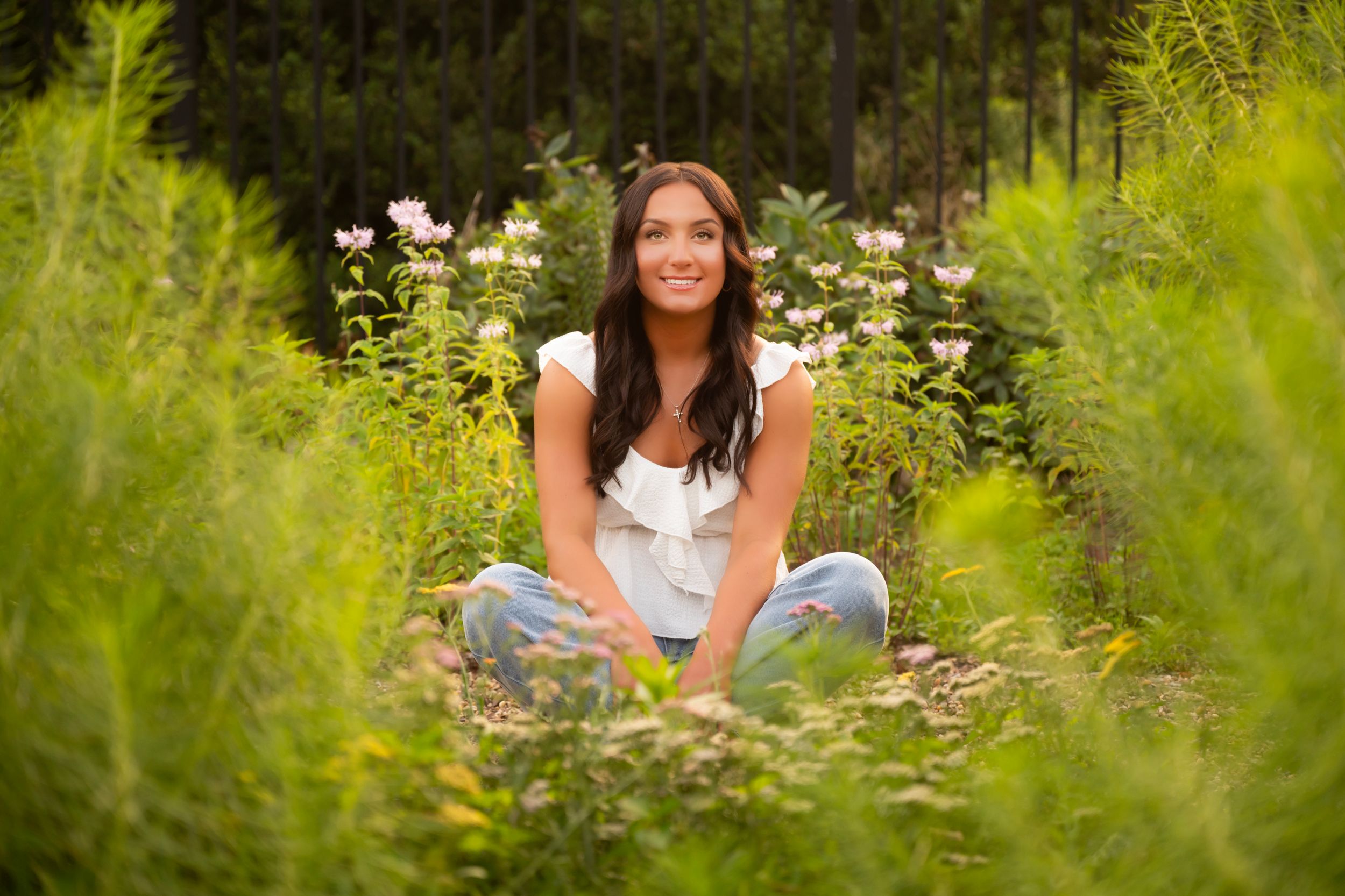 A person sits outdoors in a lush garden surrounded by blooming white daisies and green foliage.