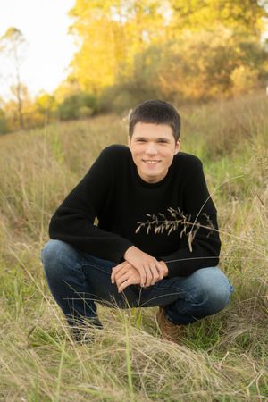Person wearing black sweater and jeans sits in autumn field with golden grasses and warm sunlight.