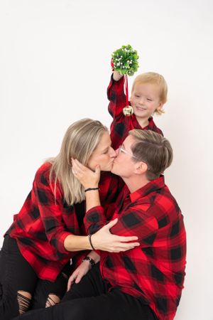 Family wearing buffalo plaid poses together with holiday decorations.