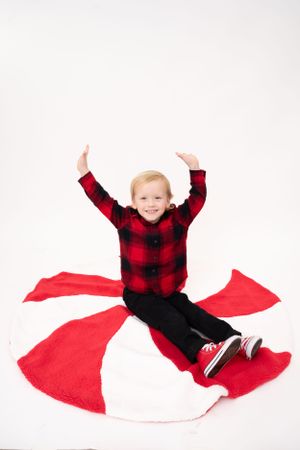 Child in buffalo plaid shirt plays on red and white circular backdrop.
