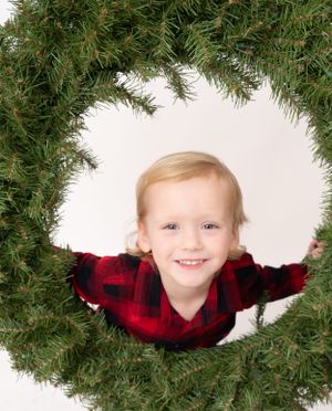 Holiday wreath frame surrounds subject wearing red buffalo plaid shirt.