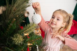 Young child decorating Christmas tree with ornaments and twinkling lights in holiday celebration setting.