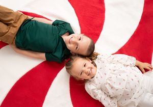 Two smiling children lying on a large red and white peppermint swirl rug during Christmas.