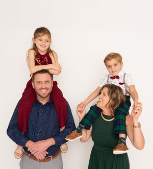 Family portrait against white background with parents and children in festive holiday attire including red and green clothing.