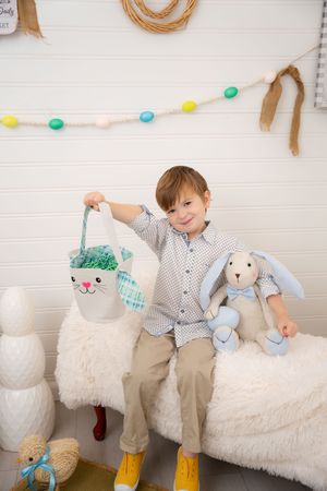 Easter themed photo session with colorful garland, plush bunny decorations, and white furry bench against white backdrop.