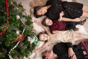 Several poses of people lying on plush carpet near a decorated Christmas tree.