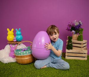 A child in blue clothing sits on artificial grass with Easter decorations including pastel bunnies and eggs in the background.