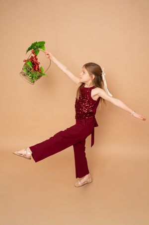 Dancer in burgundy sequined outfit leaps gracefully against beige backdrop in dynamic motion sequence.