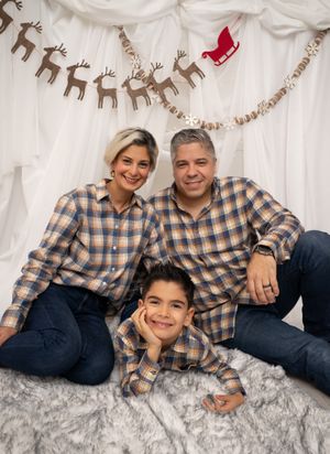 Family wearing matching plaid shirts poses together on gray fur blanket for holiday photos.