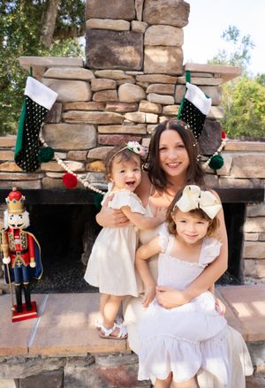 Family in white outfits sharing joyful moments together by a stone wall with holiday decorations.