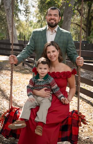 Family holiday portrait on a swing with man in green blazer, woman in red dress, and young boy in festive sweater.