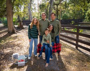 A group poses together on a wooded trail with fall leaves and wooden fencing on a sunny afternoon.