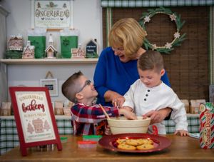 Three people baking holiday treats together in a festively decorated kitchen.