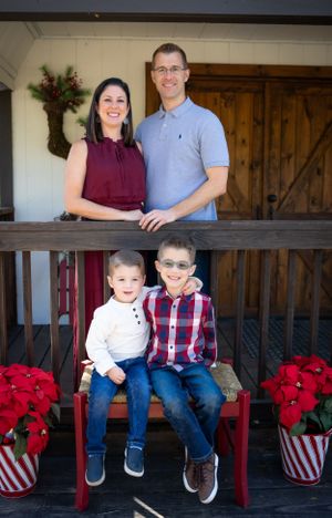 Holiday family portrait on a porch with poinsettias and wooden barn door background.