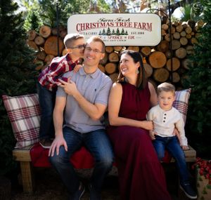A family of four poses on a bench at a Christmas tree farm for a holiday portrait.
