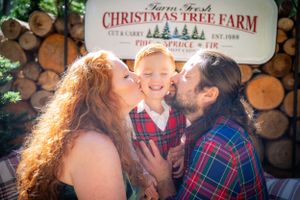 A festive family moment captured at a Christmas tree farm with stacked wood background.