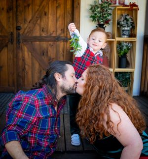 A romantic holiday moment shared between a couple while a child peeks from above.