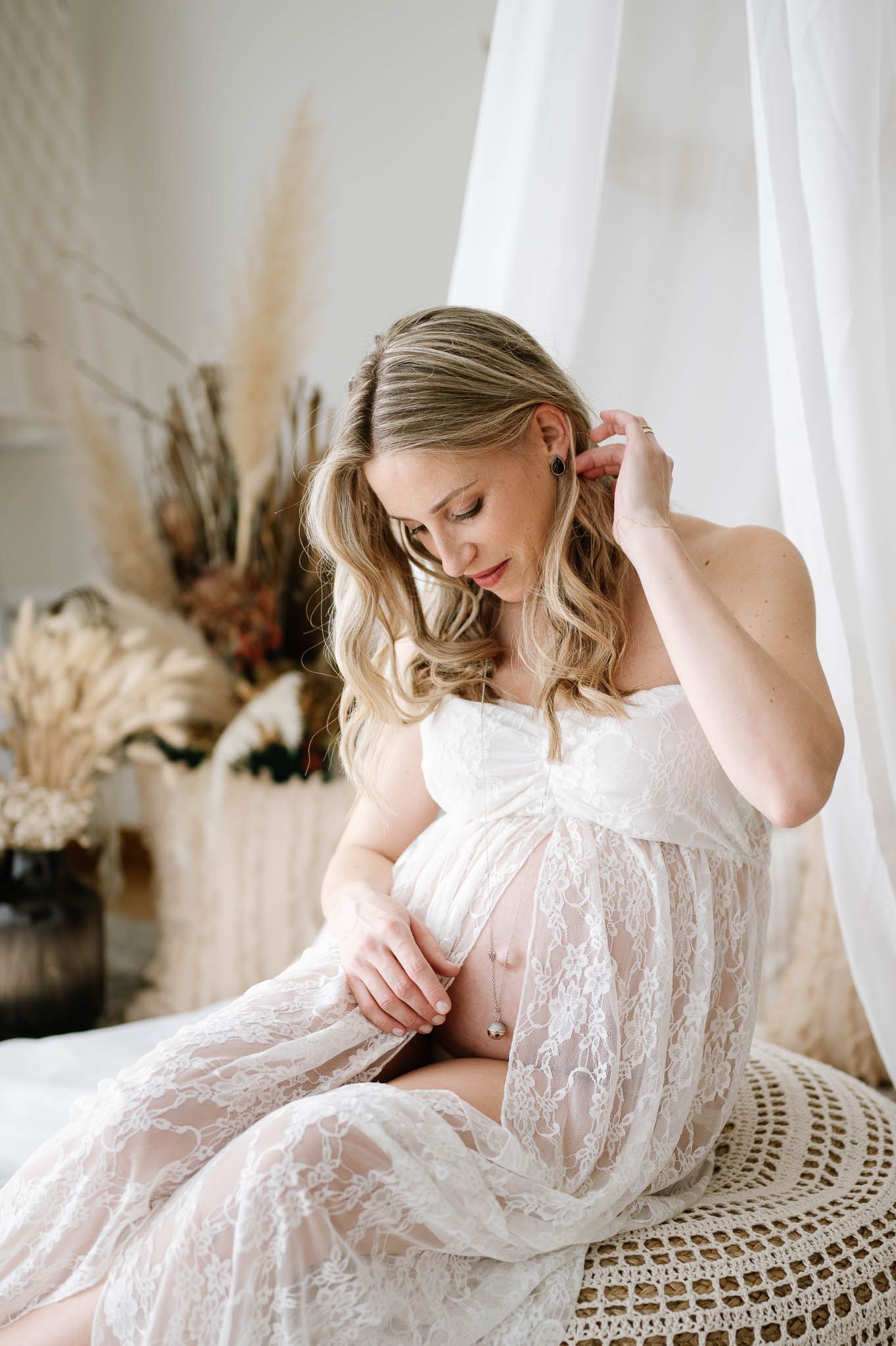 Ethereal maternity portrait featuring white lace dress and dried floral decor.