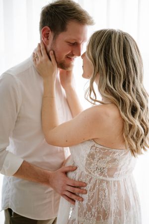 Intimate couple sharing a tender moment in white attire against a bright window backdrop.