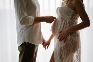 Couple in white lace and casual clothing pose together near sheer curtains.