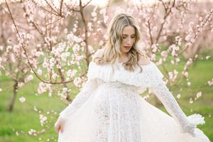Woman in white lace dress poses among blooming spring cherry blossoms.