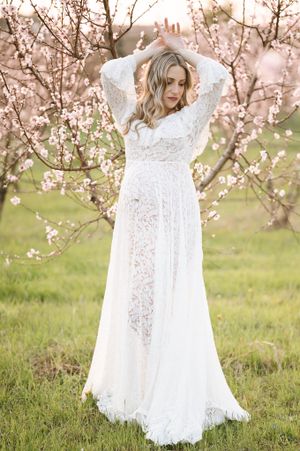 Ethereal shot of woman in flowing white lace dress amid spring blossoms.