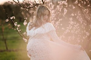 Glowing maternity portrait amid blossoming spring trees at golden hour.