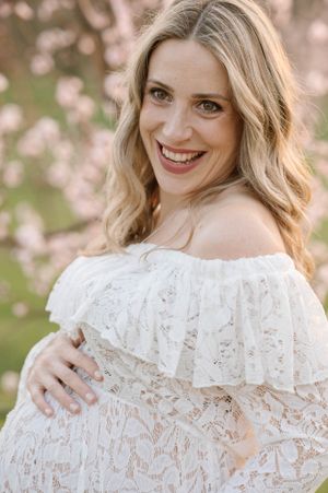 A joyful maternity portrait showcasing a white lace off-shoulder dress among cherry blossoms.