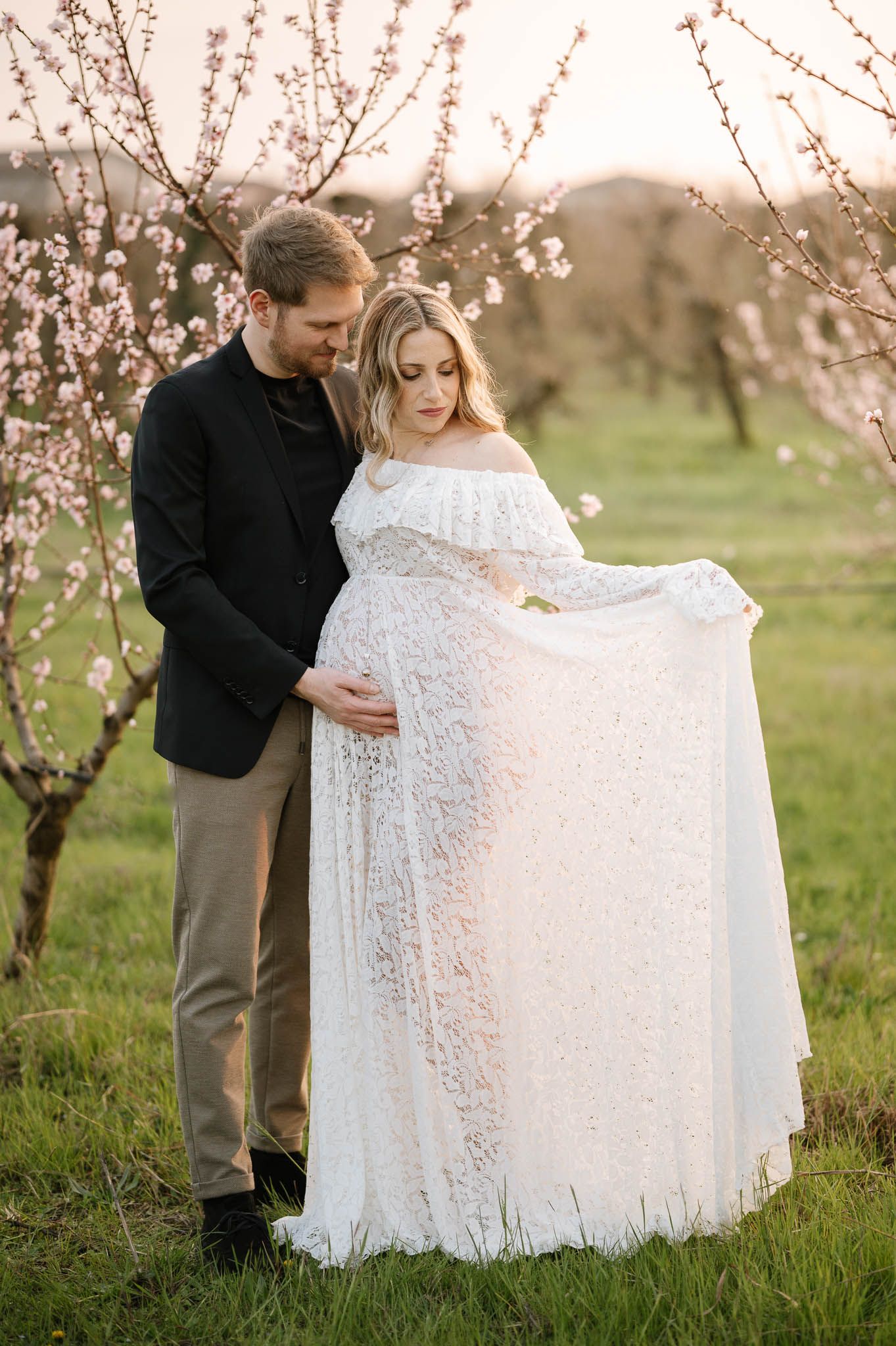 Romantic couple poses under blooming cherry trees in a spring orchard setting.