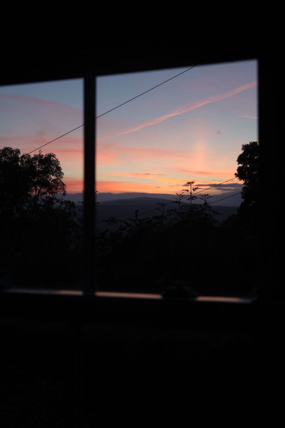 Sunset silhouette through window frames creating dark geometric shapes against orange sky.