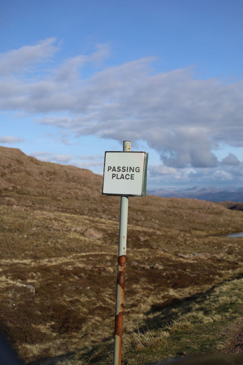 A passing place road sign stands on a remote hillside with cloudy sky in the Scottish Highlands.