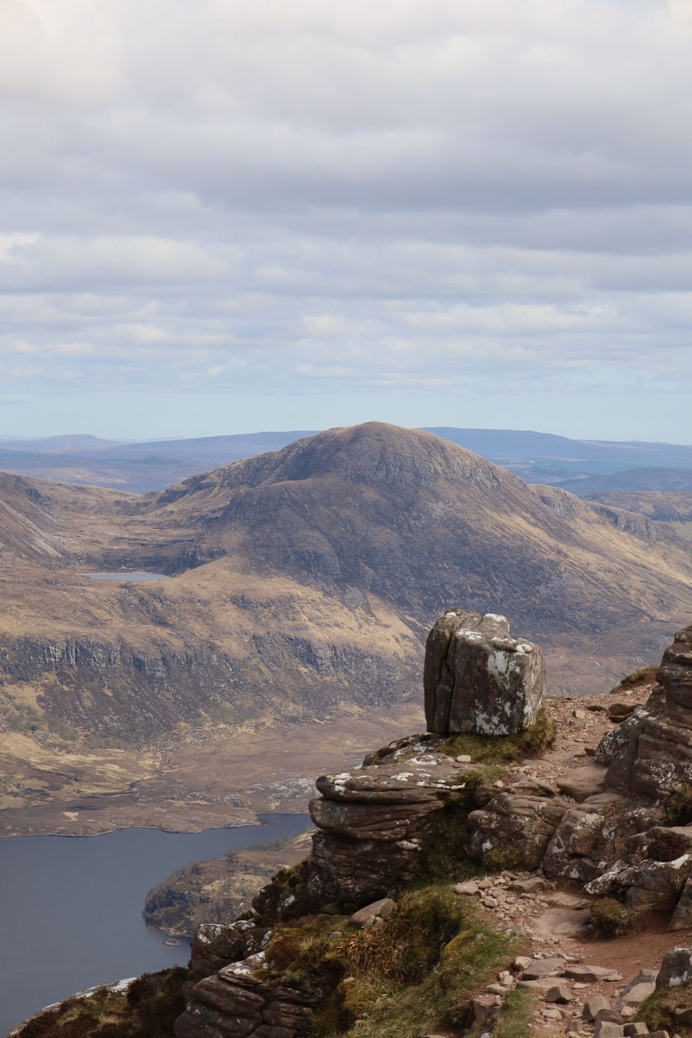 Dramatic mountain landscape with large boulder overlooking a lake in the Scottish Highlands.