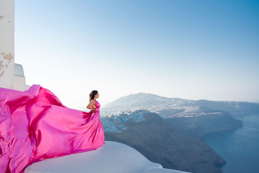 A flowing fuchsia dress creates dramatic movement against Santorini's white architecture and sea views.