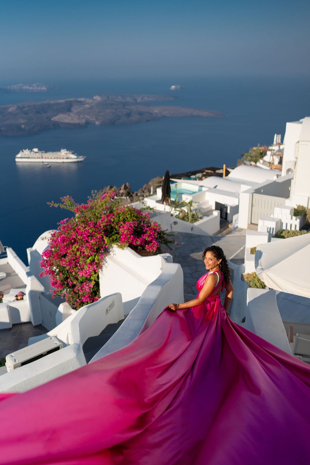 A flowing fuchsia dress creates movement against white buildings and pink flowers in Santorini.