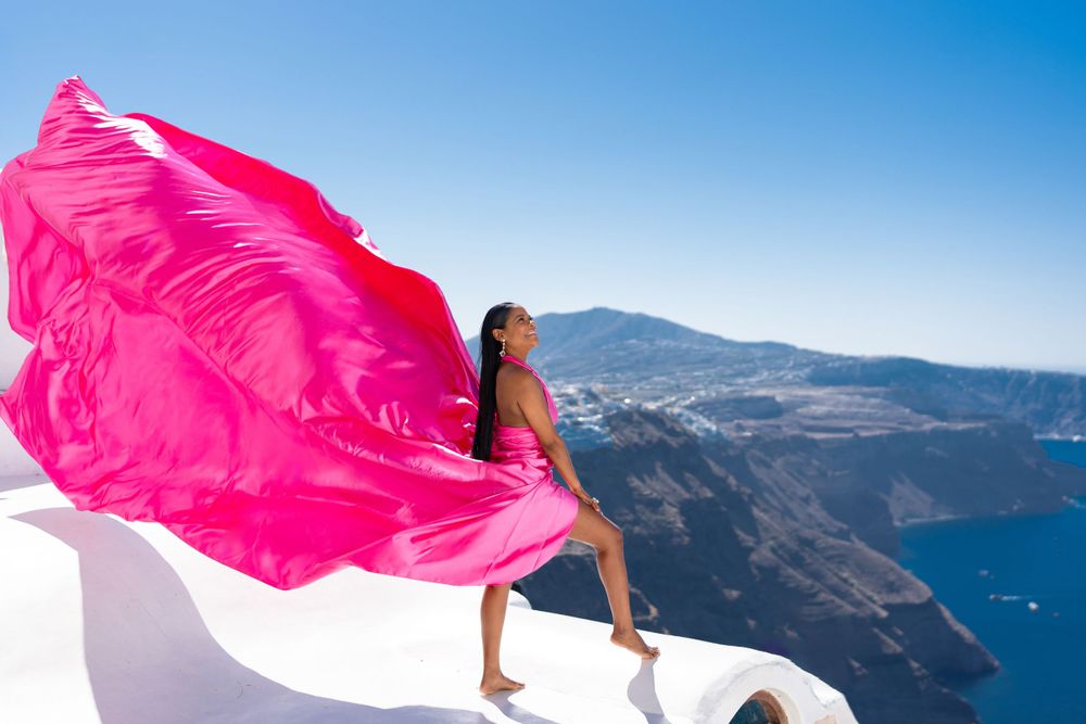 Vibrant pink fabric flows in the wind on a white rooftop overlooking the Aegean Sea.
