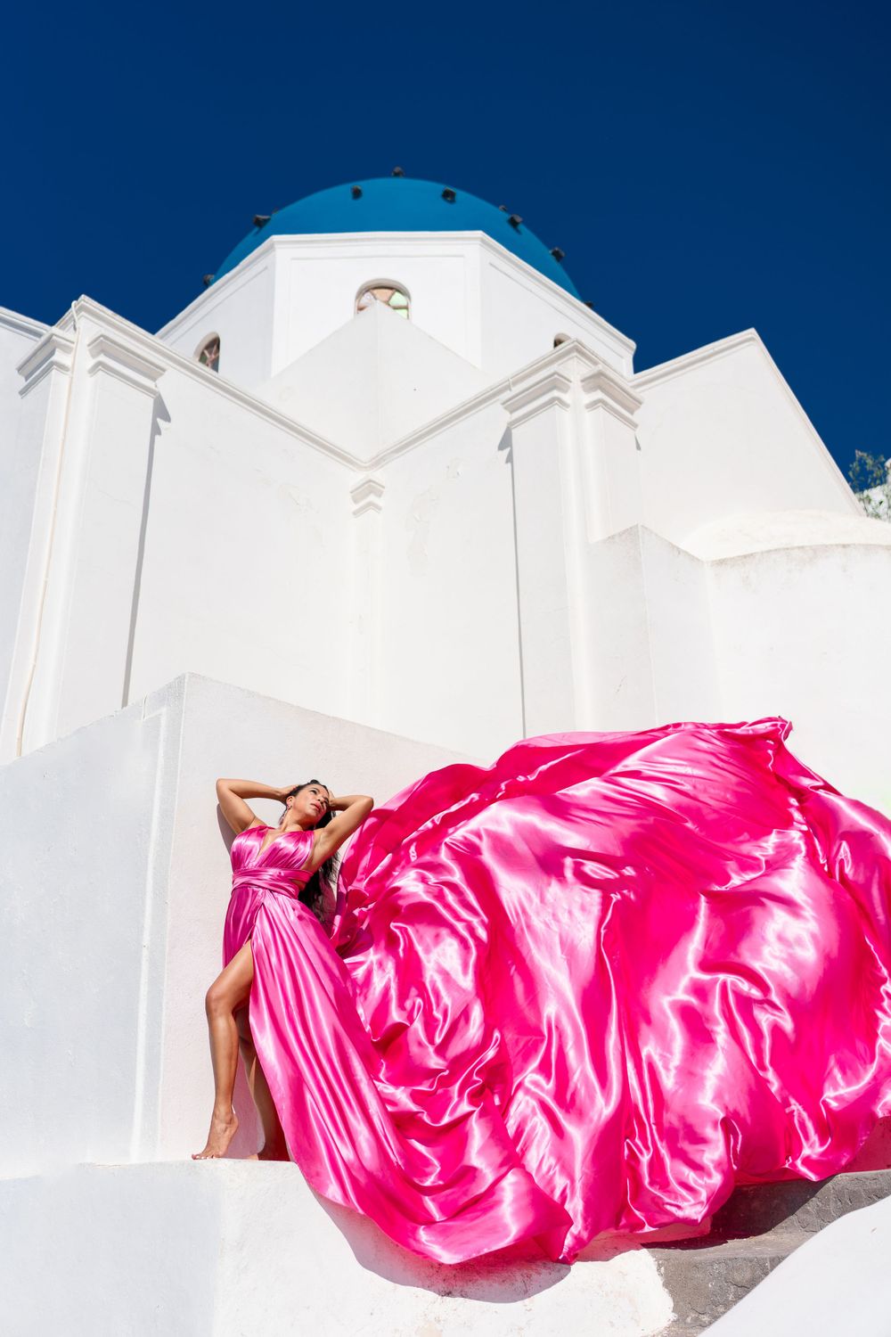 Billowing hot pink fabric creates dramatic scene against white Greek church architecture.