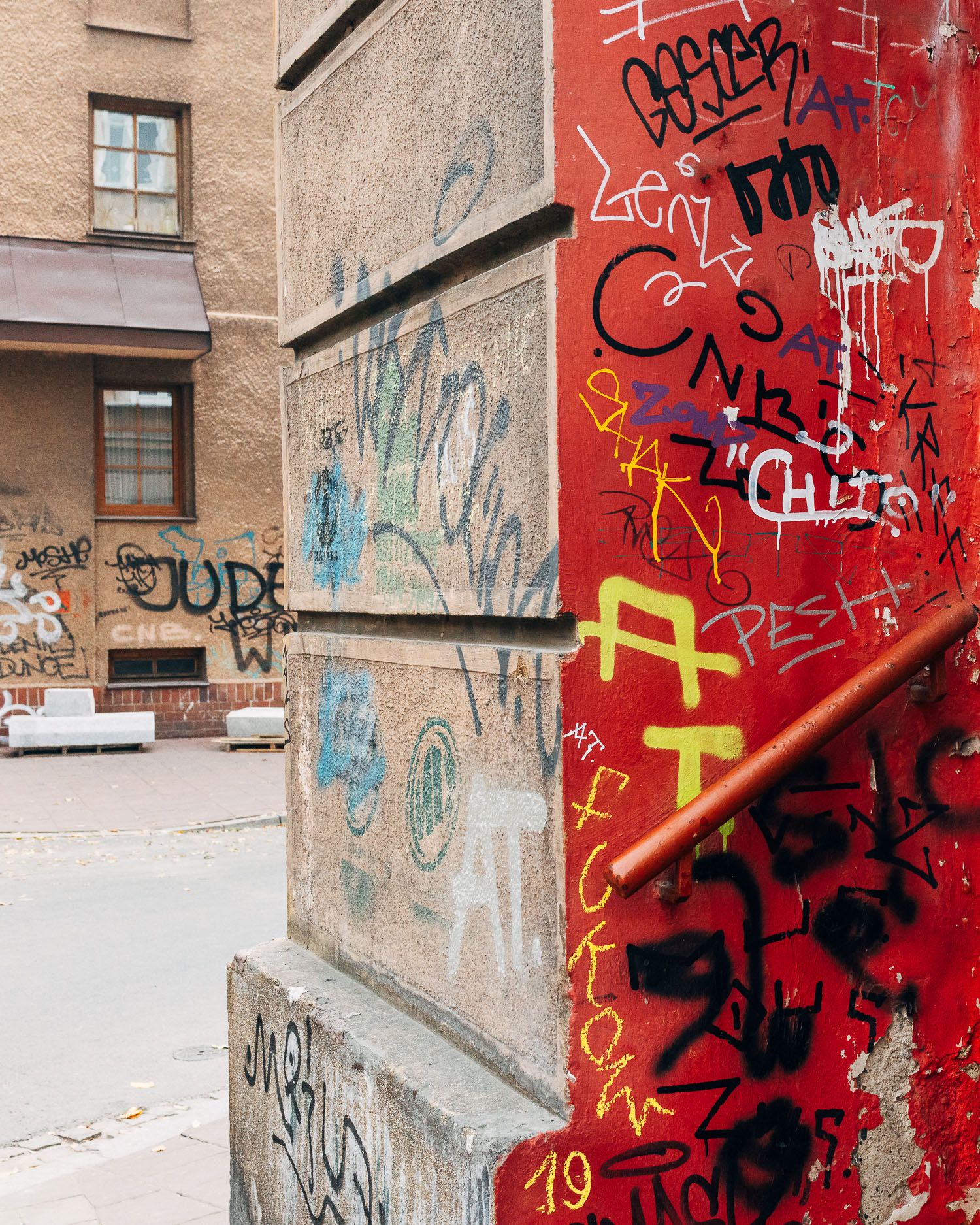 Graffiti covered red wall with concrete steps and urban decay.