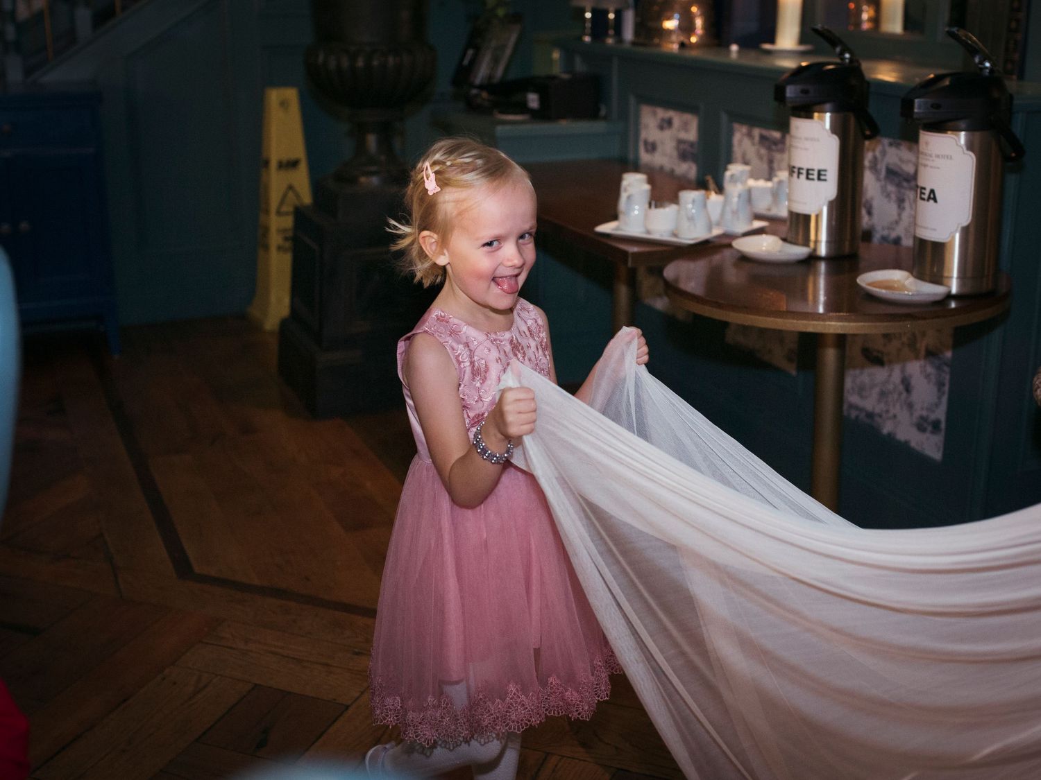 Young flower girl in pink dress playfully holding wedding dress train.