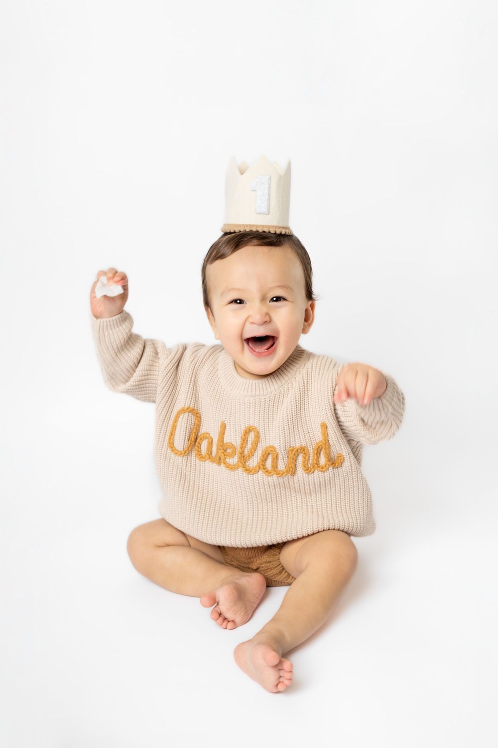 Baby wearing beige sweater with text smiles and plays on white background in three poses.