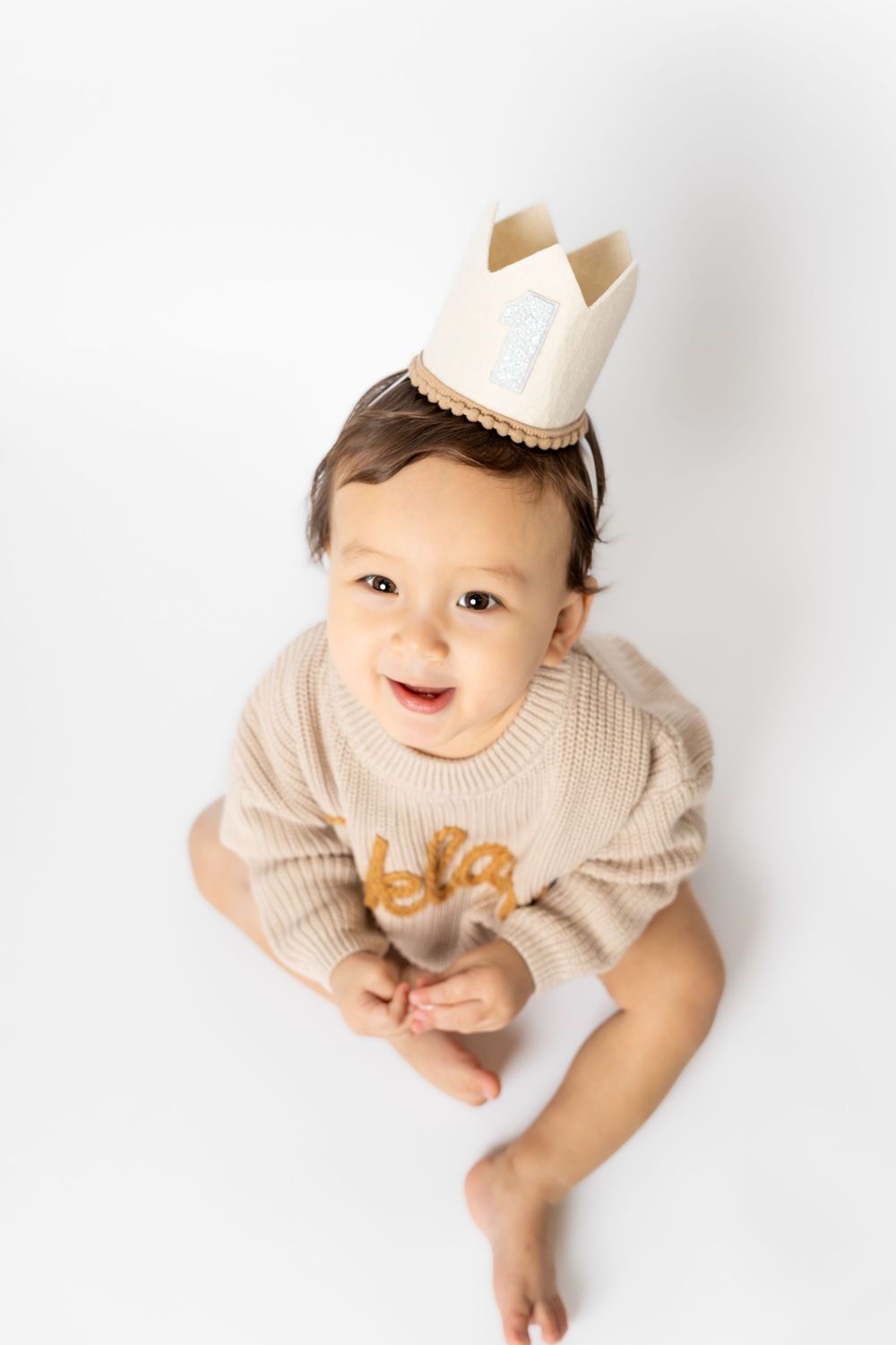 Baby in cream colored outfit and paper crown crawls on white background in three poses.