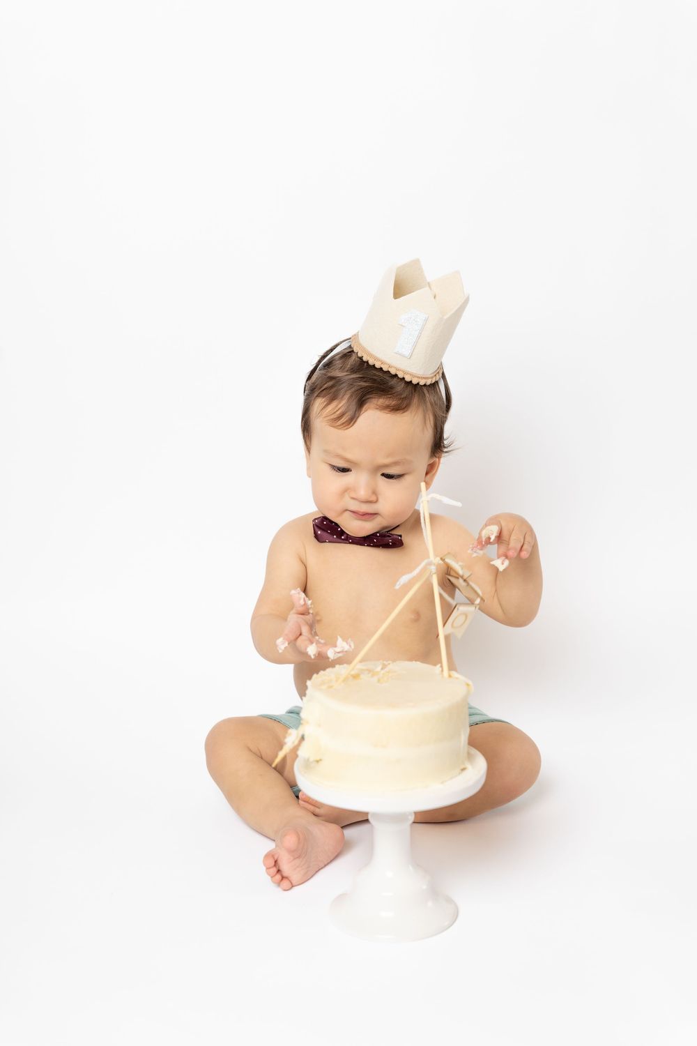 Three sequential photos show a baby in a diaper exploring and playing with a small white cake.