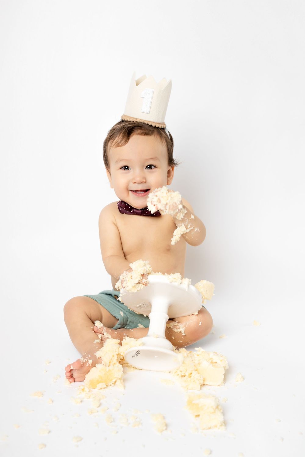 Baby playing with cake and making a joyful mess during cake smash photo session on white backdrop.