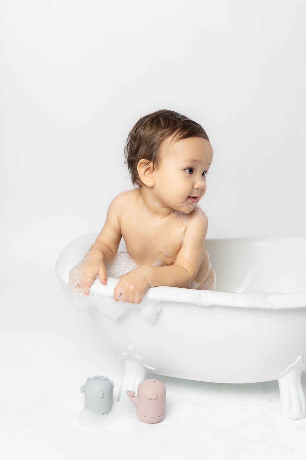 A baby sits in a white bathtub with a minimalist white background creating a clean and serene bathing scene.