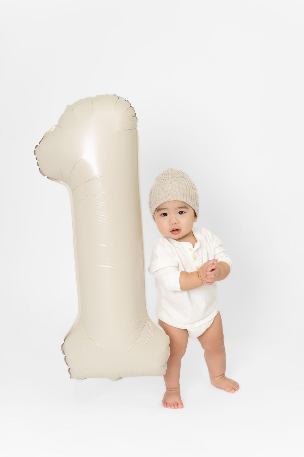 A small child in white clothing and hat poses with a large cream-colored number one decoration in multiple views.