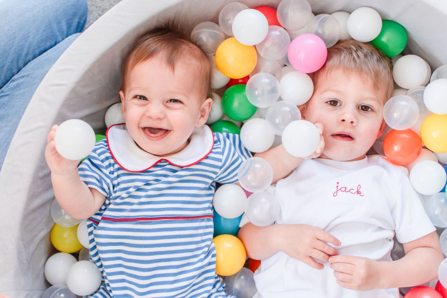 Two brothers smile, surrounded by balls from their ball pit.